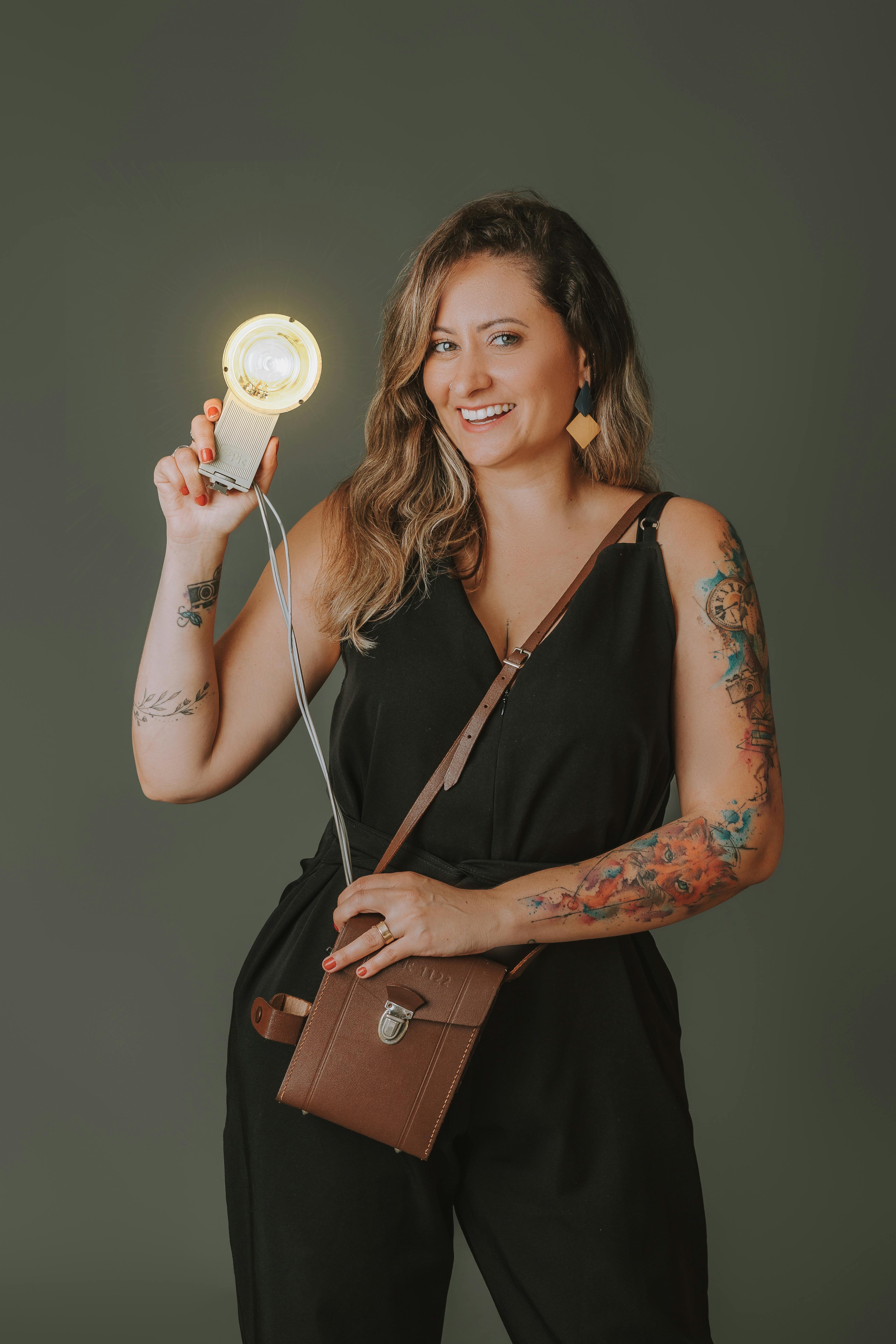 A stylish woman posing indoors with a glowing portable light, showcasing tattoos.
