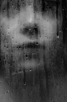 Abstract portrait of a woman's face obscured by raindrops on a glass pane.