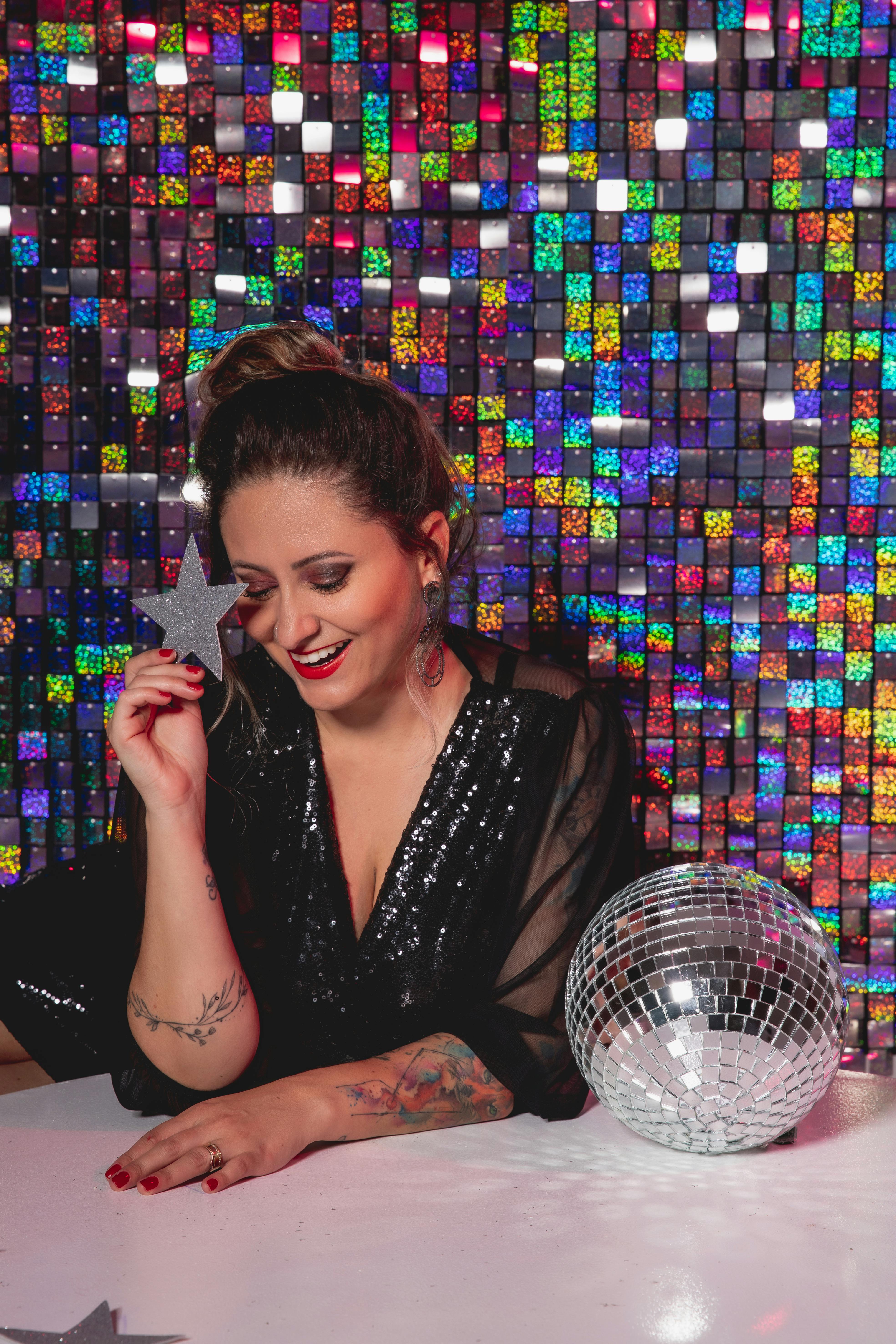Stylish woman poses with a disco ball against a sparkling backdrop, exuding glamour and enjoyment.