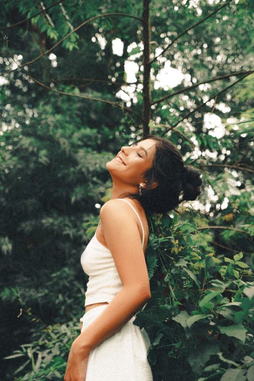 Free Young woman in white embracing nature with a serene smile in a lush forest setting. Stock Photo