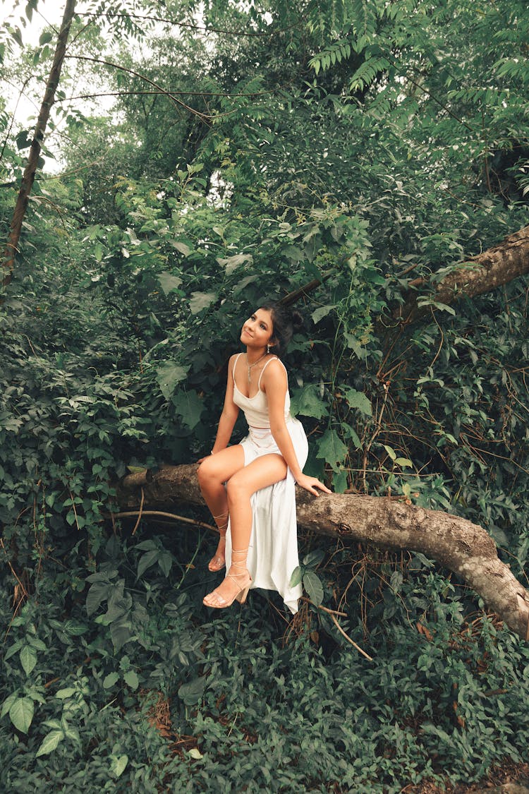 Girl Sitting On Tree Trunk In Green Forest