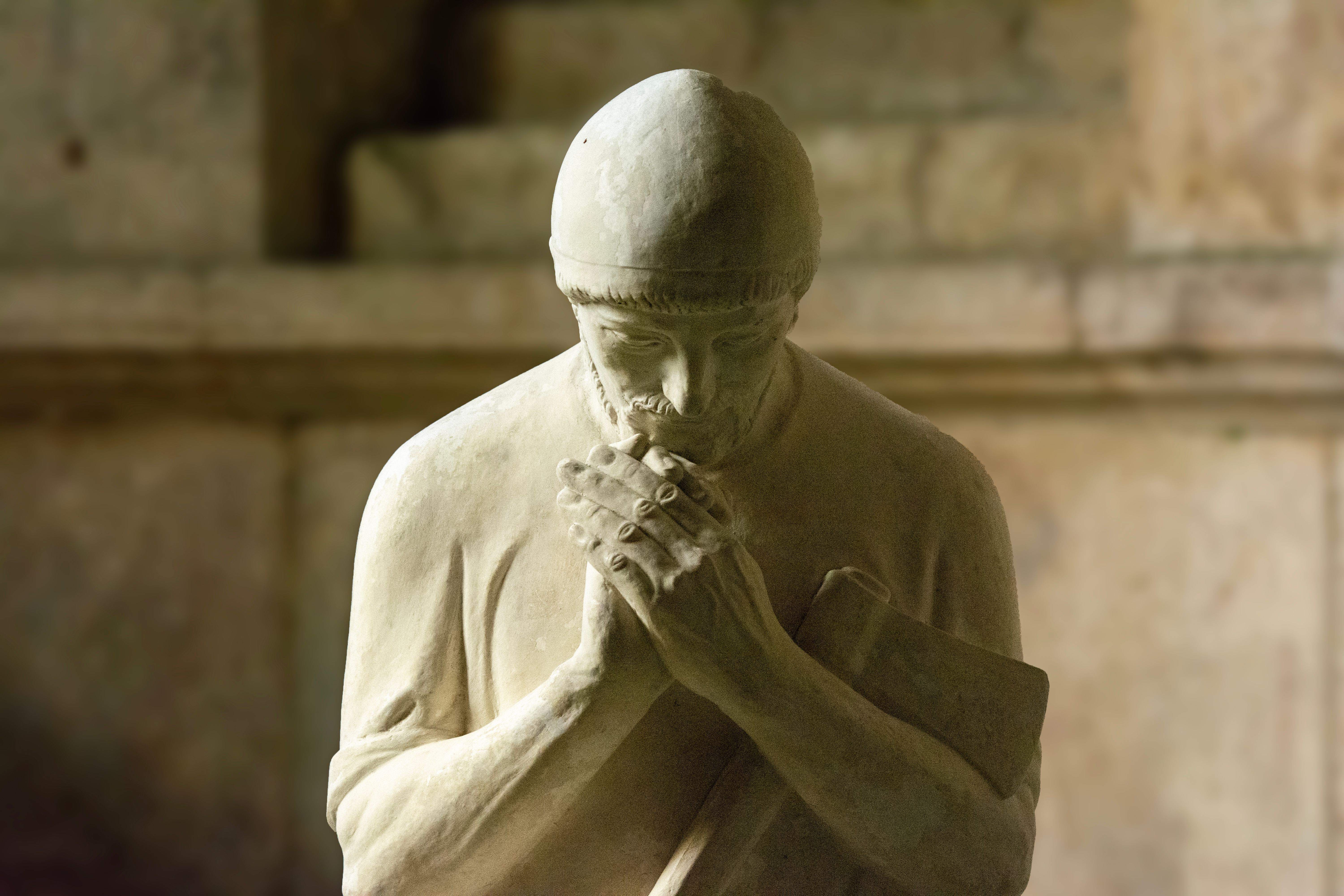 Close-up of a marble statue depicting a man in deep contemplation, hands clasped.