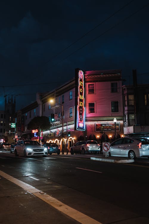 Free A street scene with cars parked in front of a neon sign Stock Photo