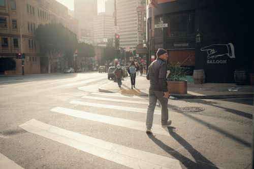 Free Man crossing a city street at a crosswalk, casting a long shadow on a sunny day. Stock Photo