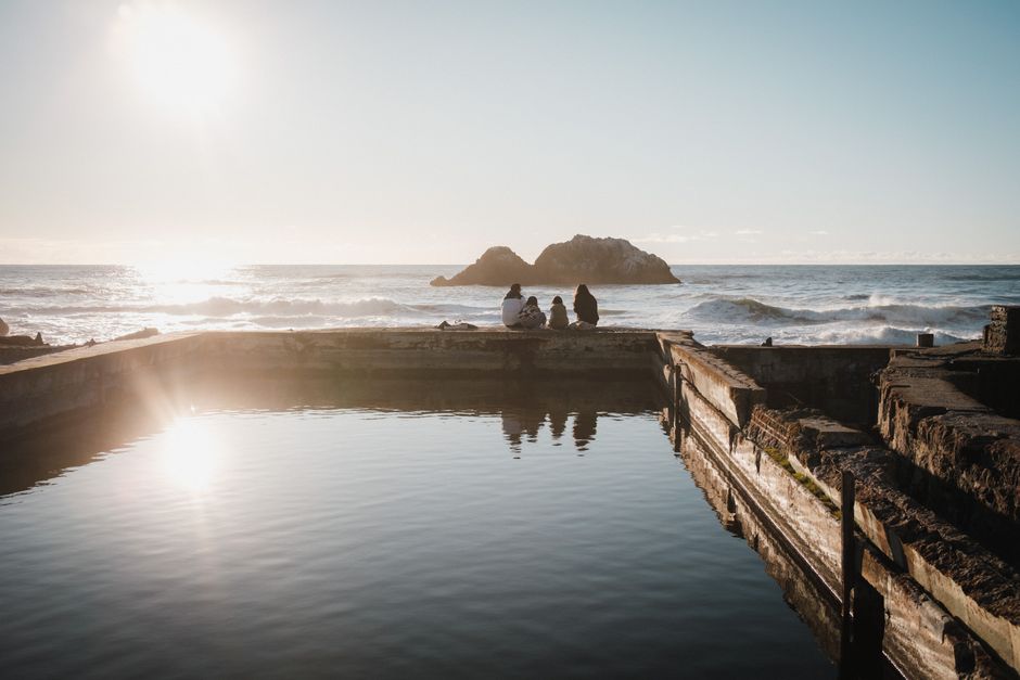 Three people enjoy a peaceful ocean view during sunset by the coast.
