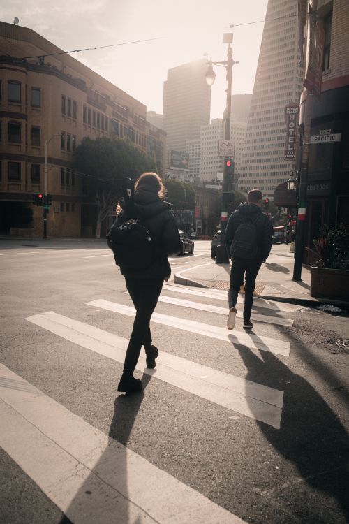 Free Two people crossing a city street at sunrise in an urban setting with skyscrapers. Stock Photo