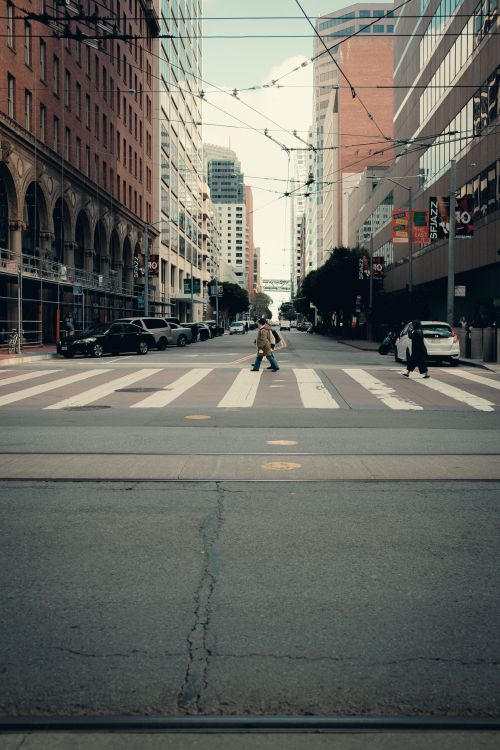 Free A typical city street view with pedestrians crossing, surrounded by urban buildings. Stock Photo