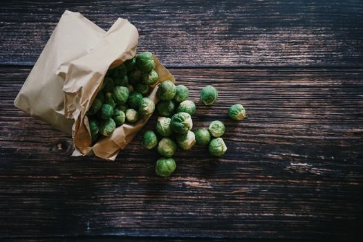 Fresh Brussels sprouts poured from a paper bag onto a rustic wooden table.