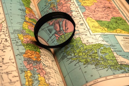 Close-up of a Magnifying Glass Lying on an Opened Book with a Map 
