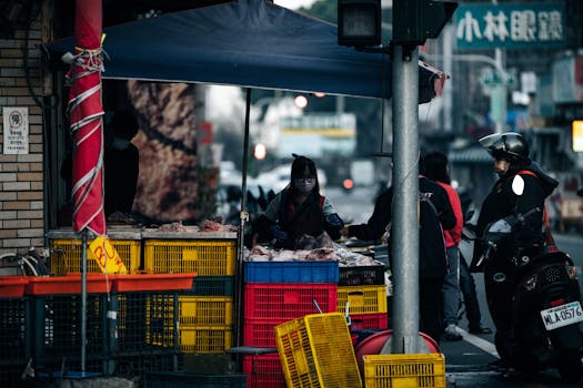 Busy street market scene with vendors and customers engaging at outdoor stalls.