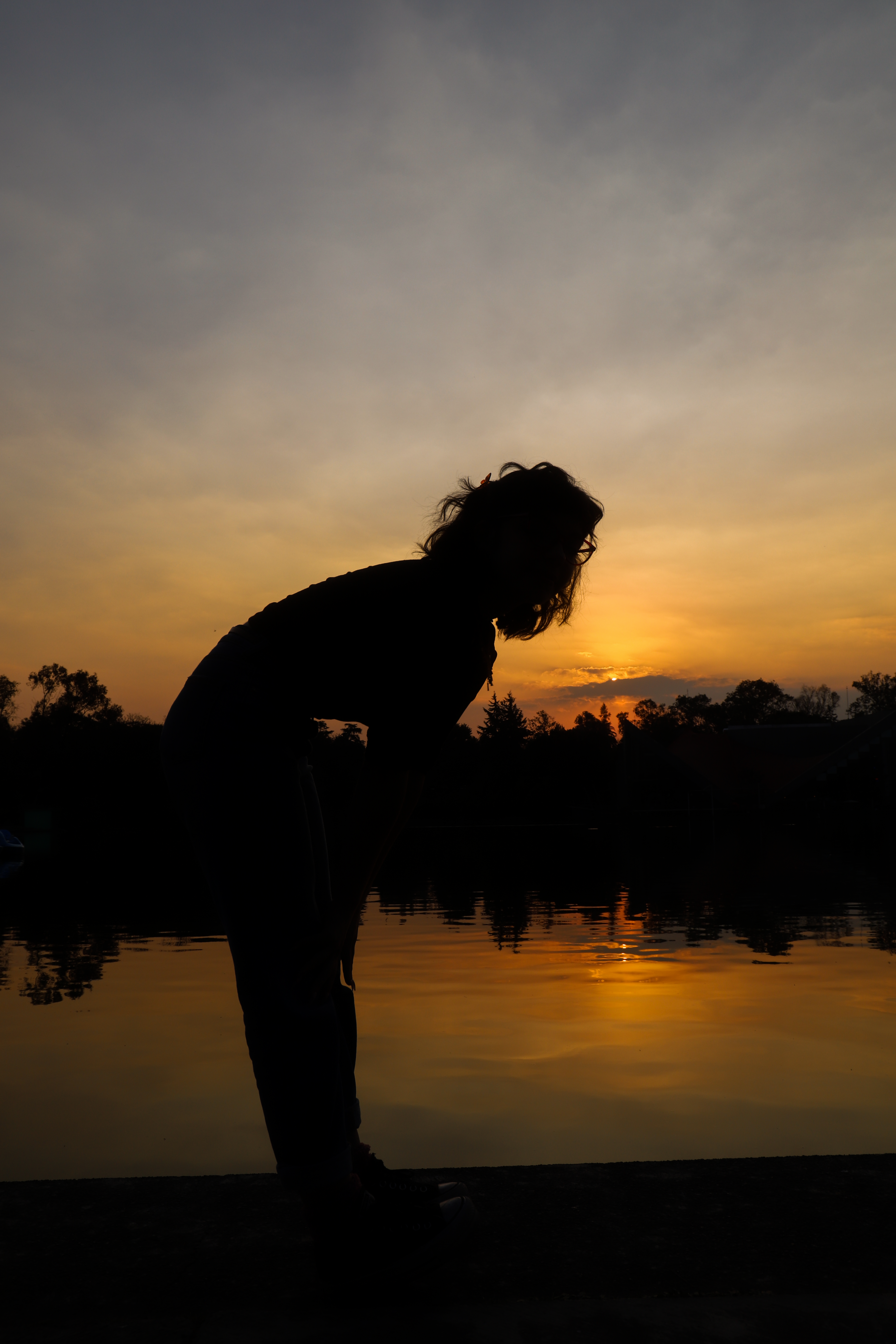 Fotomural Una mujer silhouetada contra un vibrante atardecer en la orilla de un lago en la Ciudad de México, México.