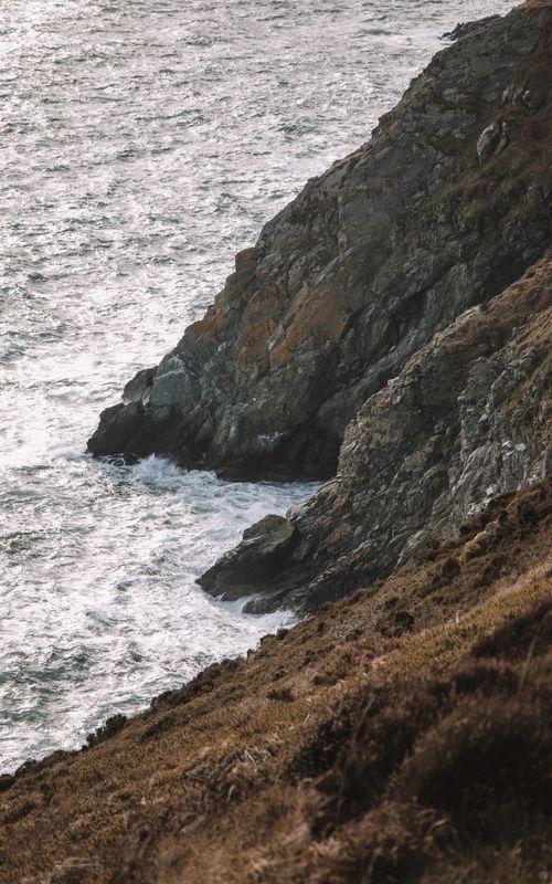 Free Dramatic view of rocky cliffs and ocean waves at sunset along Dublin's coastline. Stock Photo