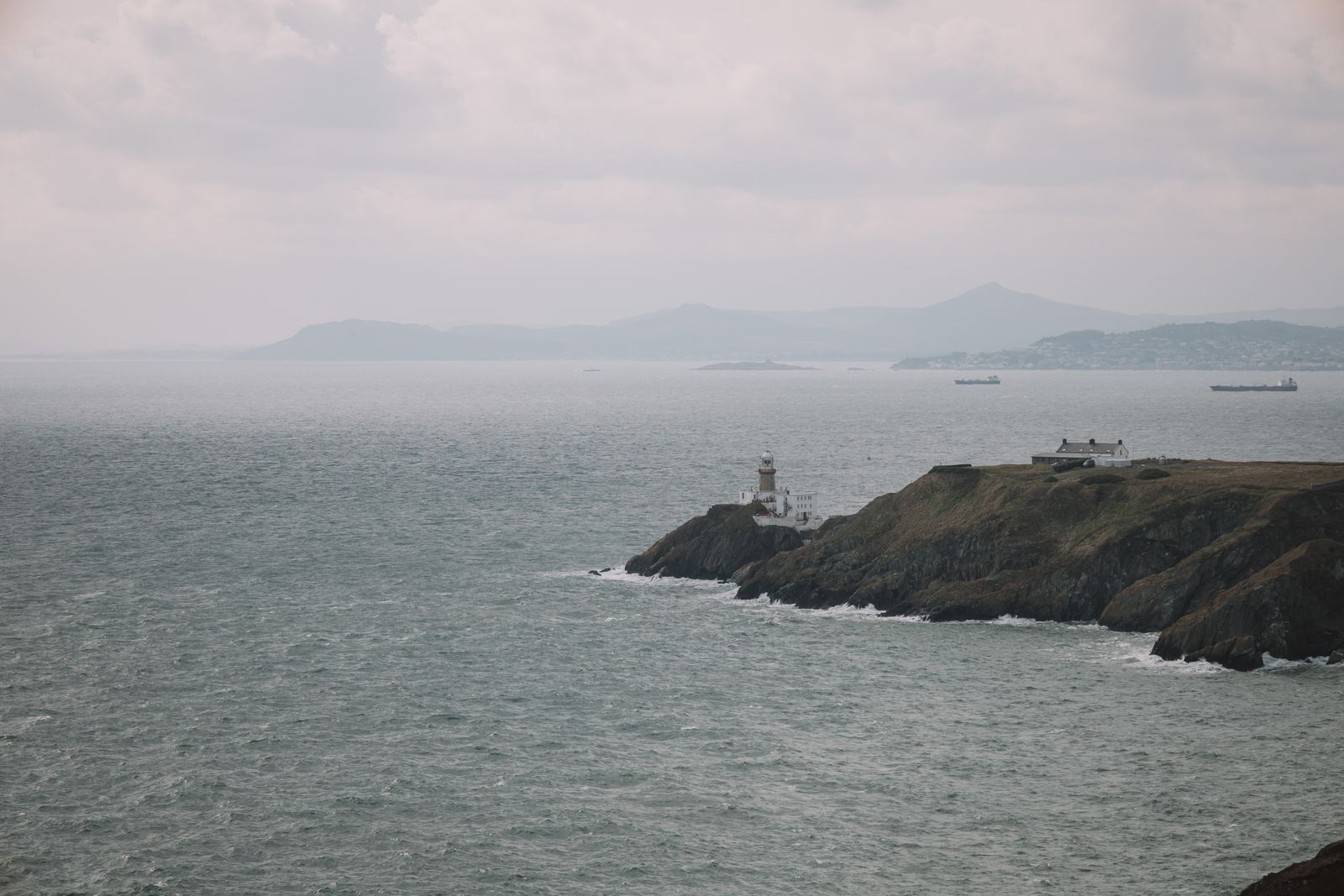 View of Dublin's Baily Lighthouse amidst fog and gentle waves, capturing Ireland's rugged coastline