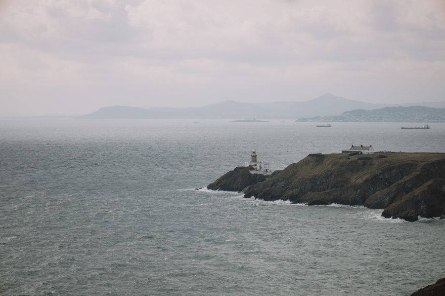View of Dublin's Baily Lighthouse amidst fog and gentle waves, capturing Ireland's rugged coastline