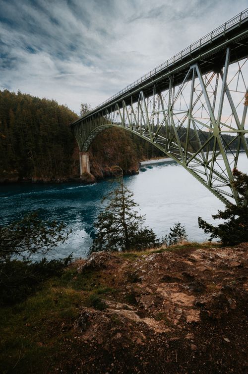 Free Suspension bridge spanning a tranquil river amidst lush mountains and vibrant nature, offering a picturesque view. Stock Photo