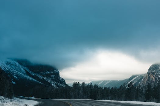 A scenic winter road winding through misty mountains and dense forest in Revelstoke, Canada.