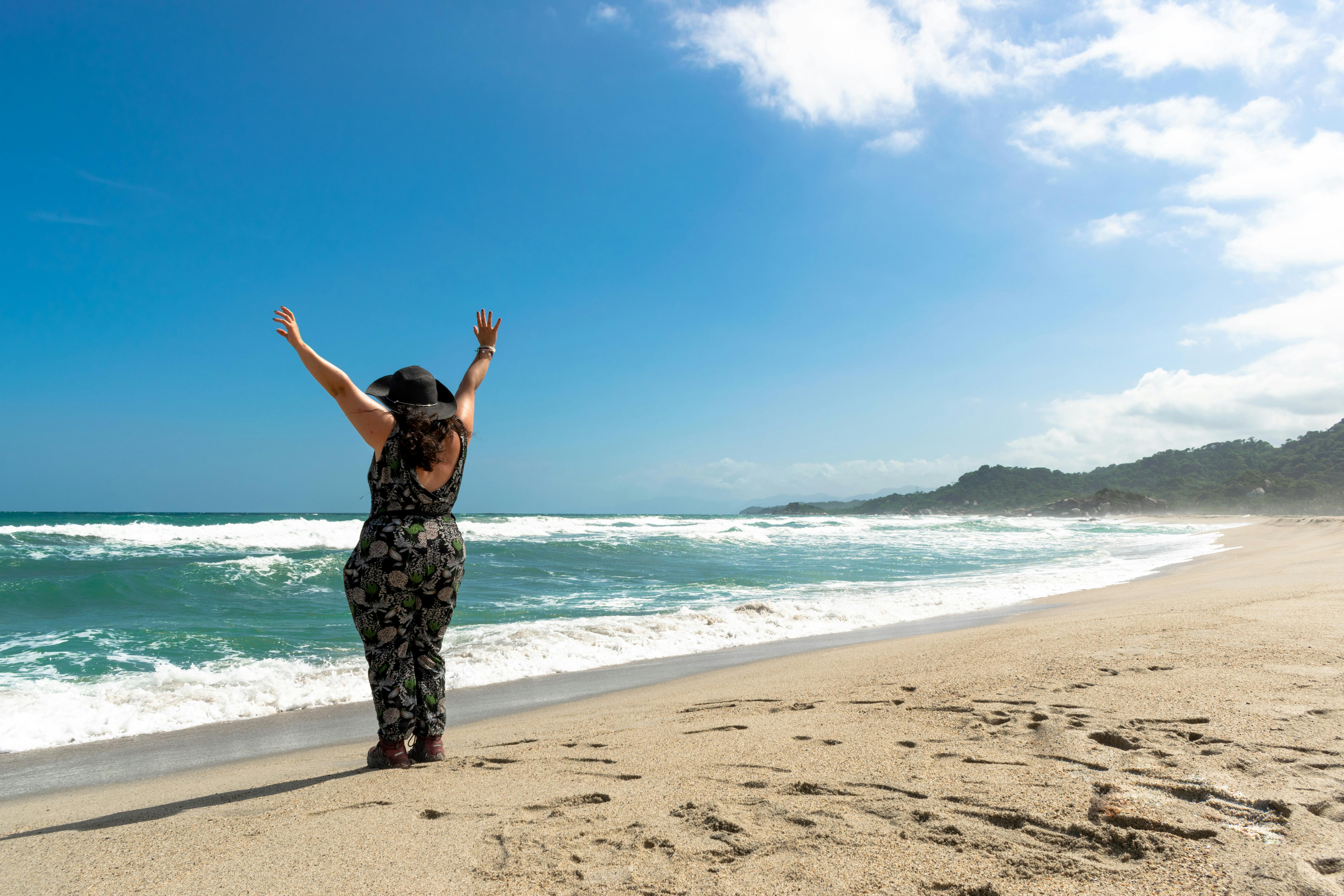A woman with raised arms enjoys a sunny day on Santa Marta's beautiful beach.