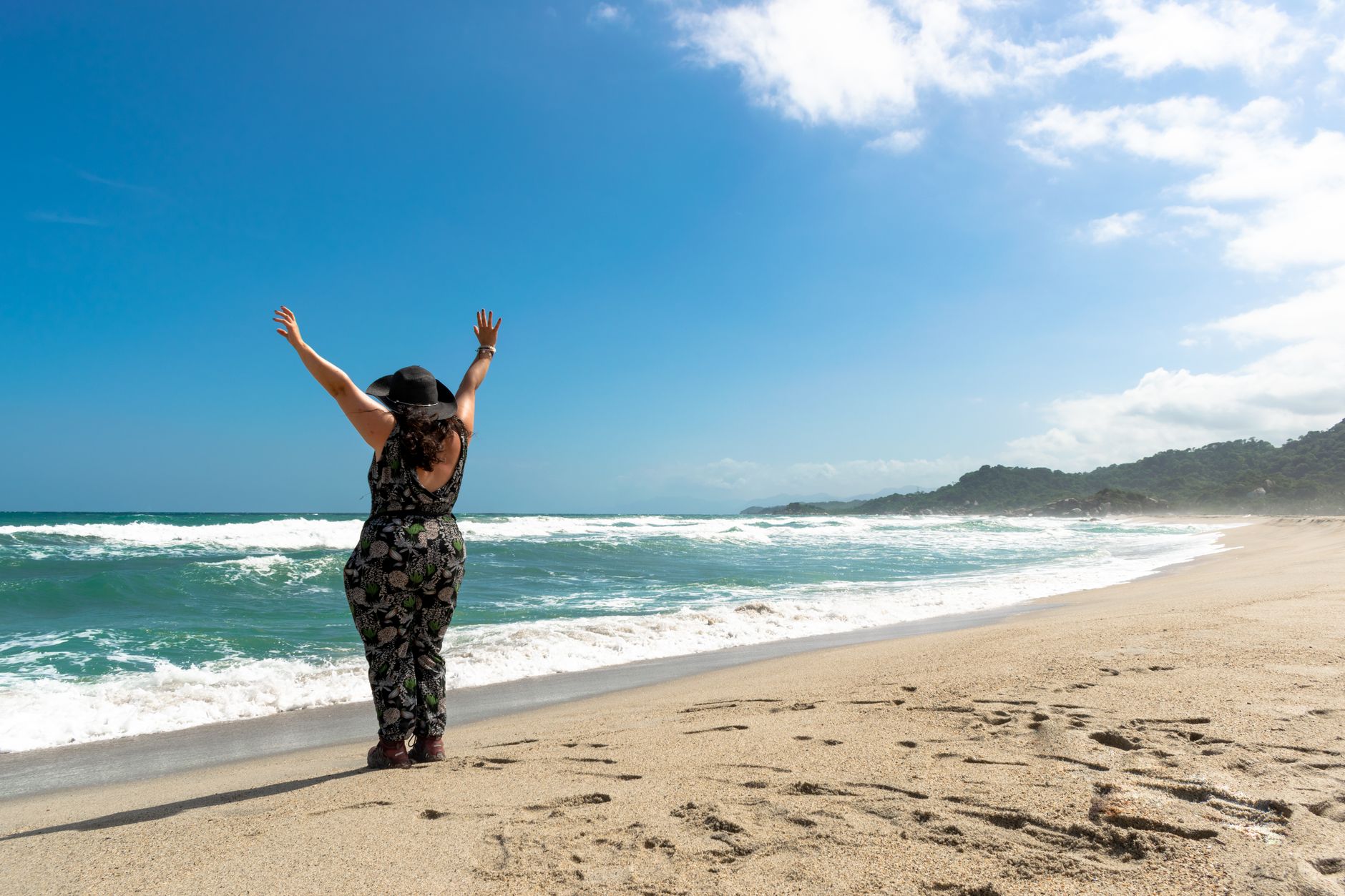 A woman with raised arms enjoys a sunny day on Santa Marta's beautiful beach.