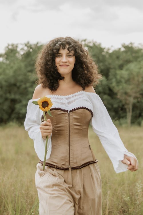 Young Woman Wearing a Dress with a Corset Walking on a Field with a Flower 