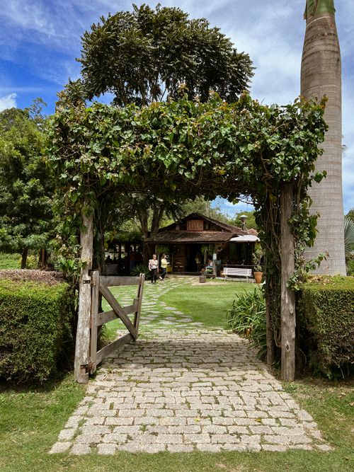 Free A rustic garden entrance leading to a countryside house with vibrant greenery and a blue sky. Stock Photo