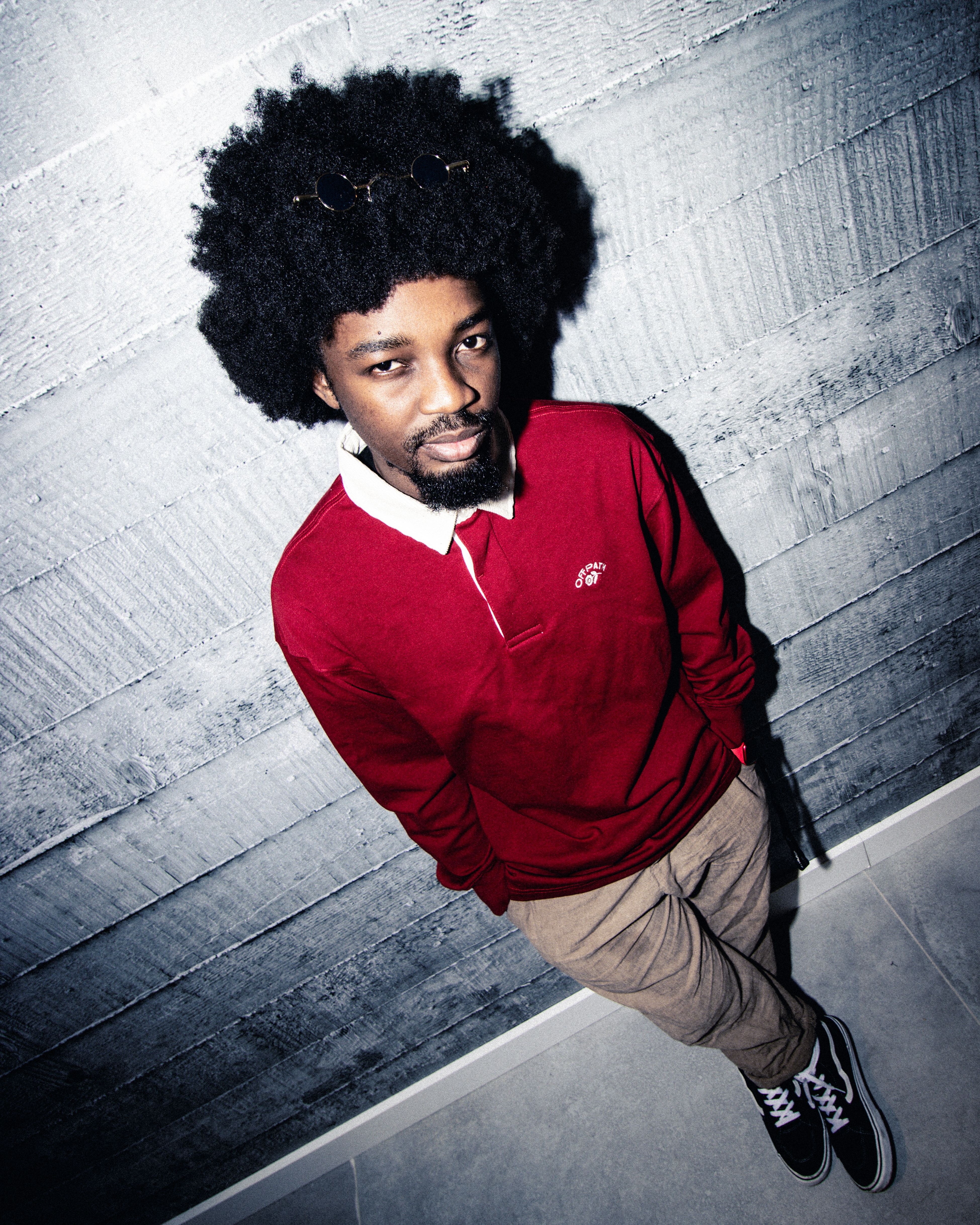 Fashion portrait of a cool man in a red polo shirt leaning against a concrete wall, captured in Budapest.
