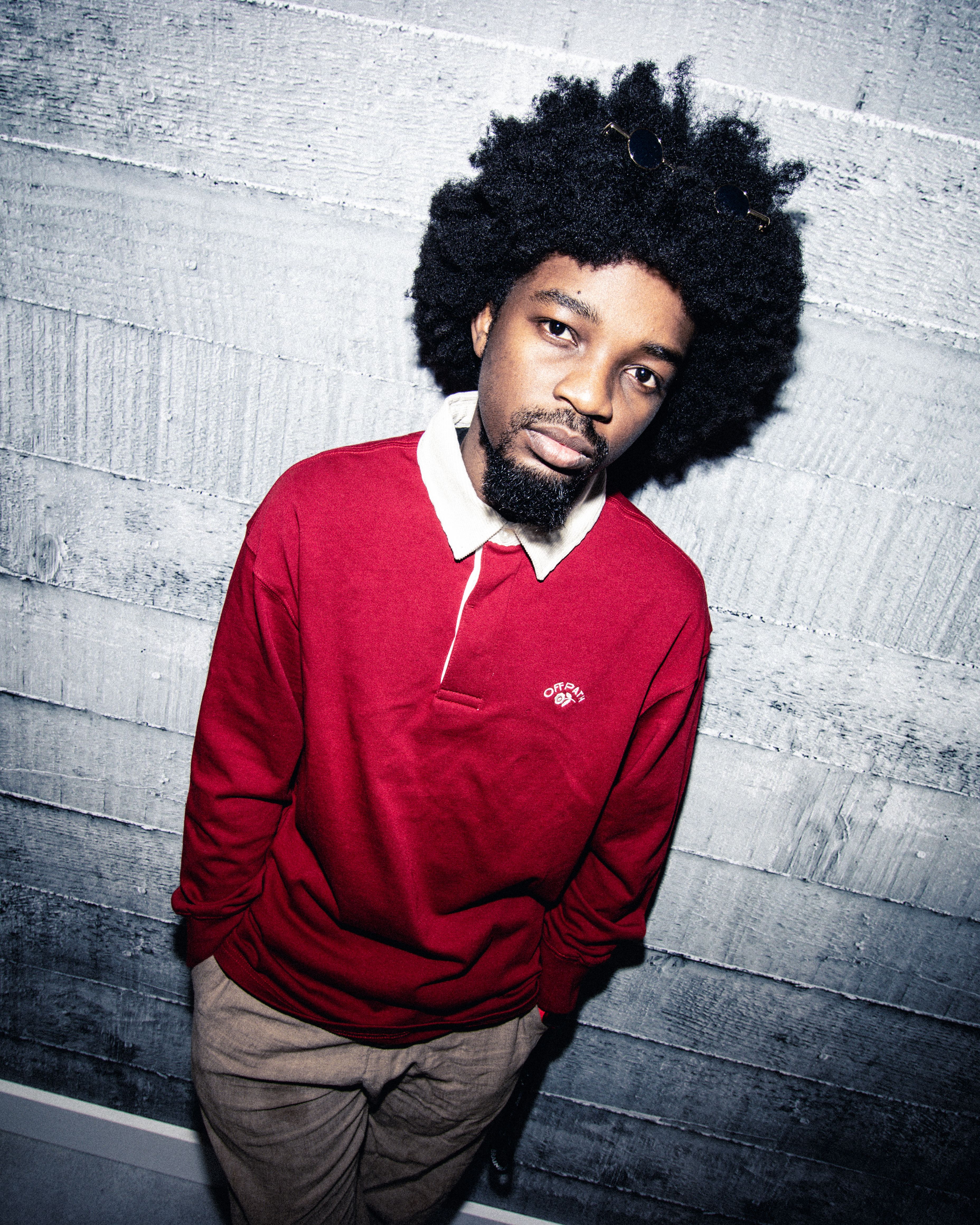 Cool man with afro hair in red sweater poses against concrete wall in Budapest.