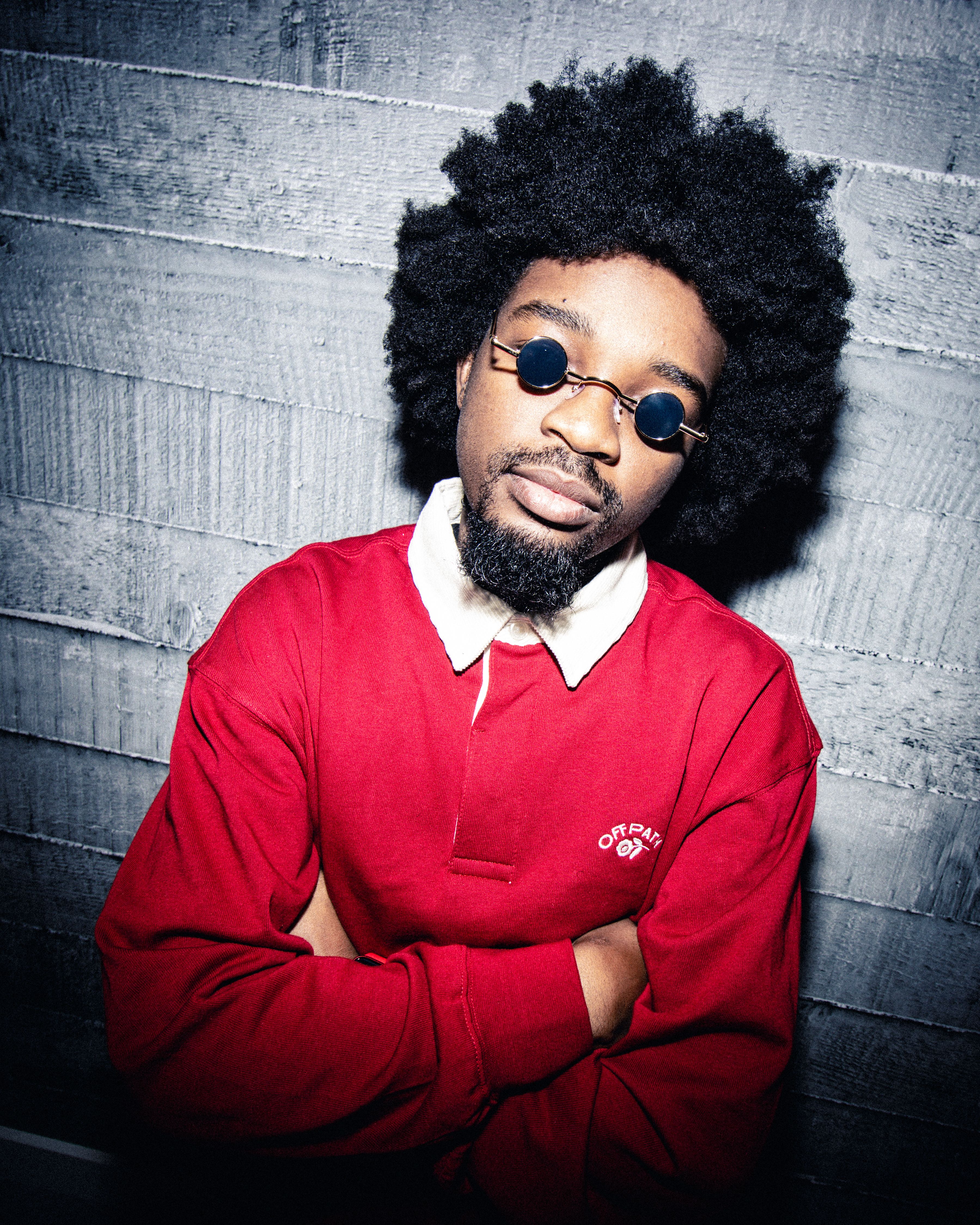 Portrait of a fashionable Black man in a red outfit with sunglasses, showcasing bold style.