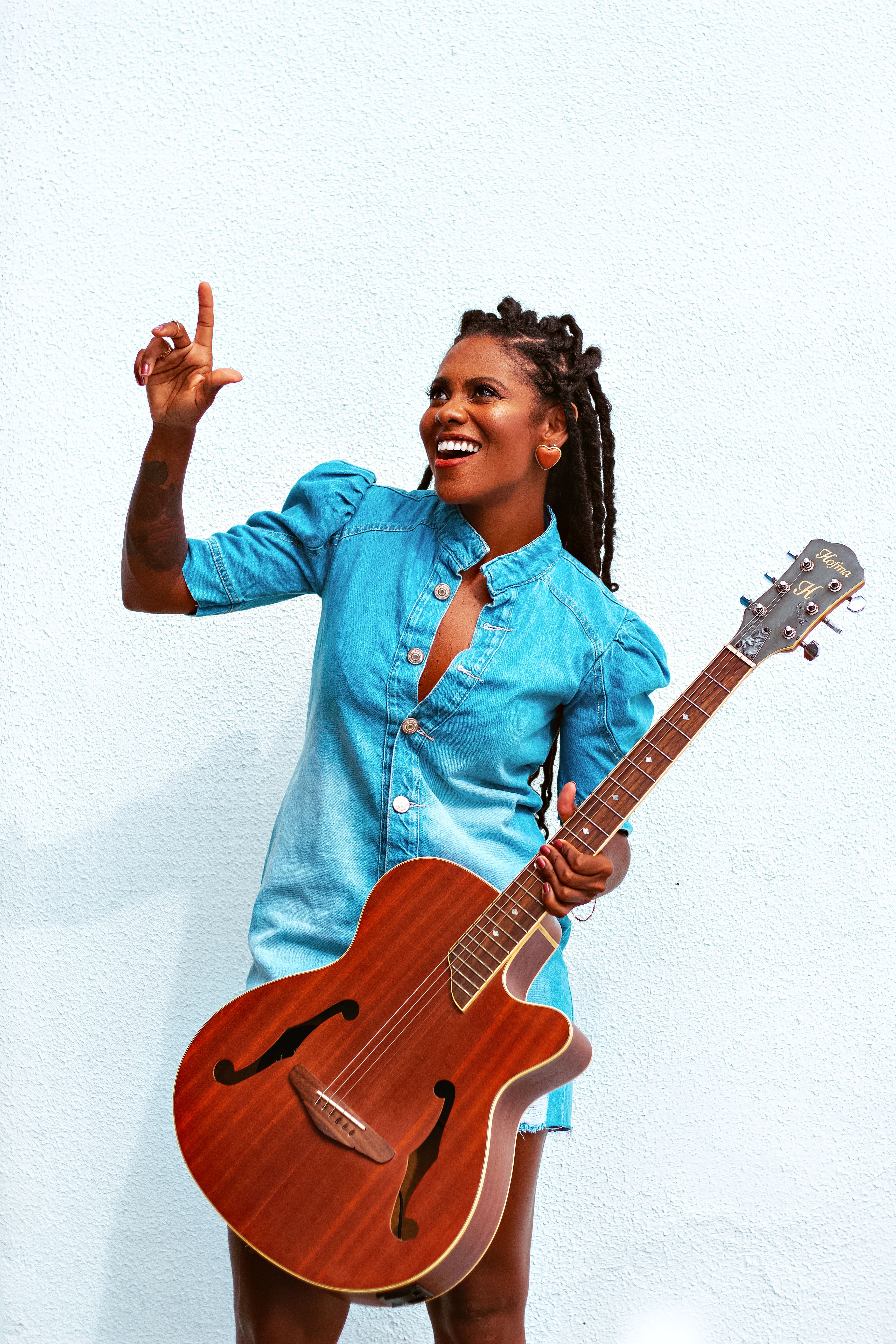 Happy woman with dreadlocks playing guitar against a white wall.