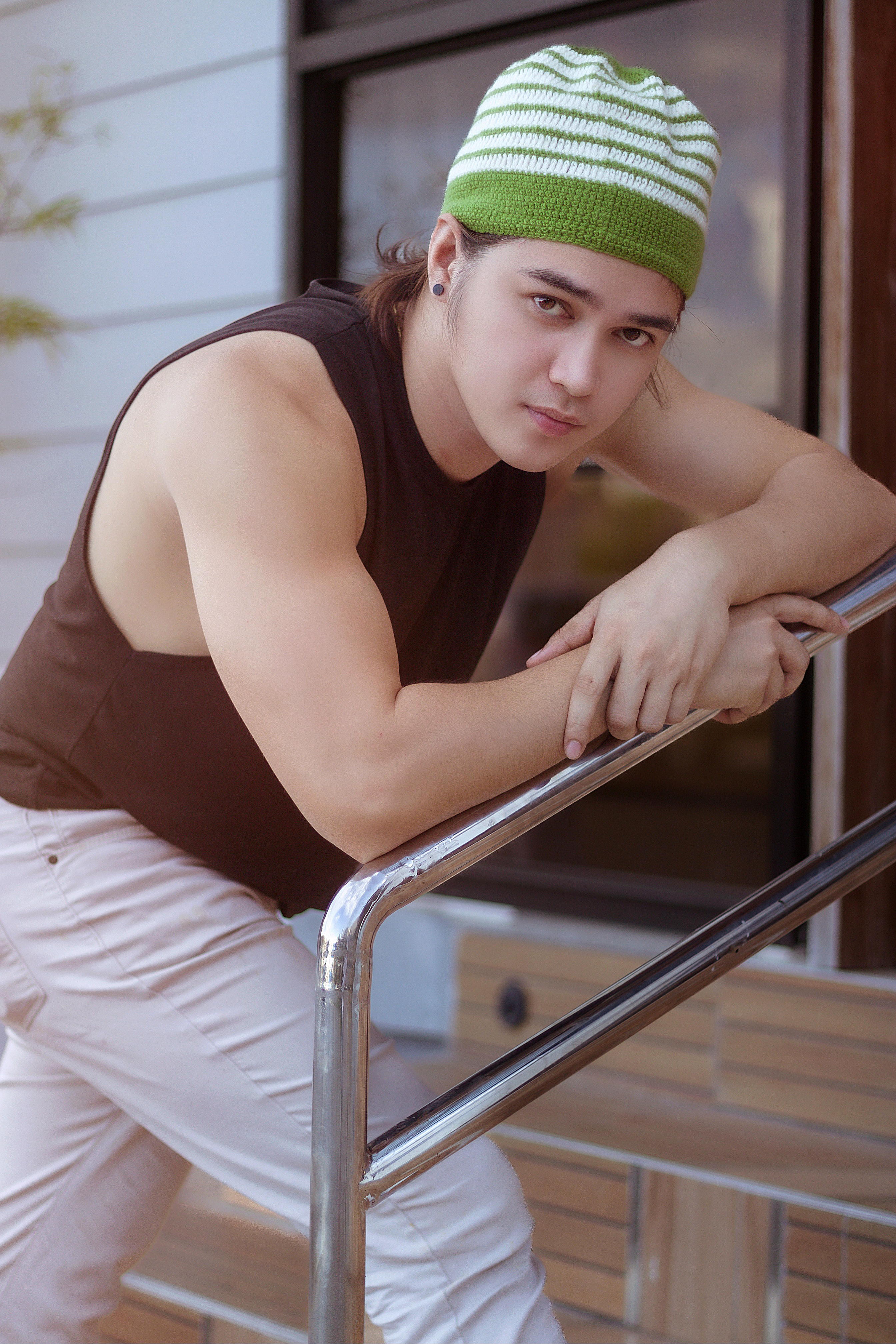 Young man in casual attire with a knit hat leaning on a handrail outdoors.