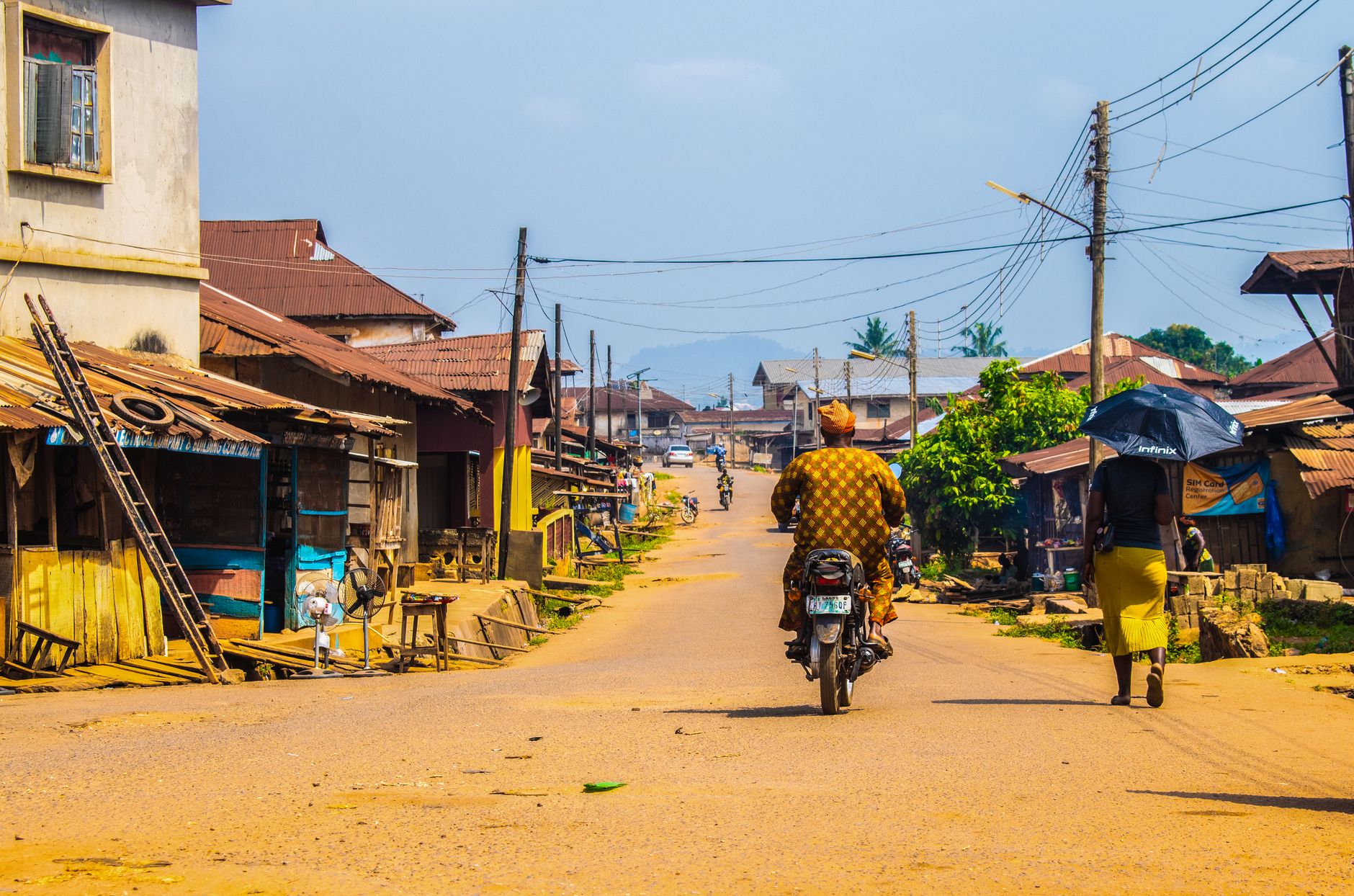 Colorful street scene with a motorcycle and pedestrian, capturing daily life in an African village.