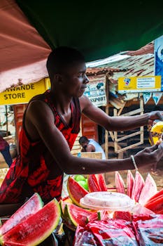 A vendor offers fresh watermelon slices at a bustling outdoor market.
