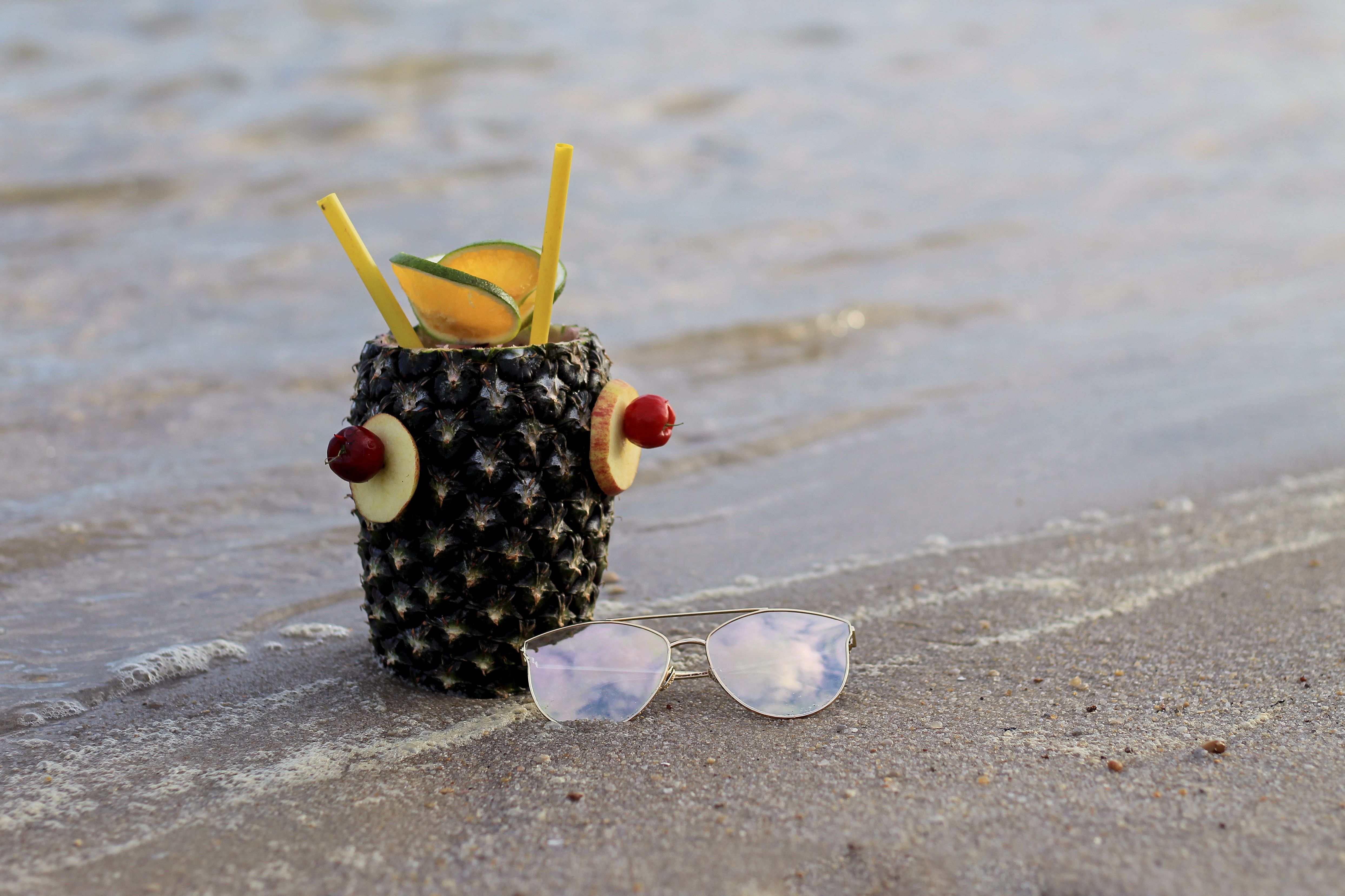 Tropical pineapple drink with sunglasses on the beach shoreline.