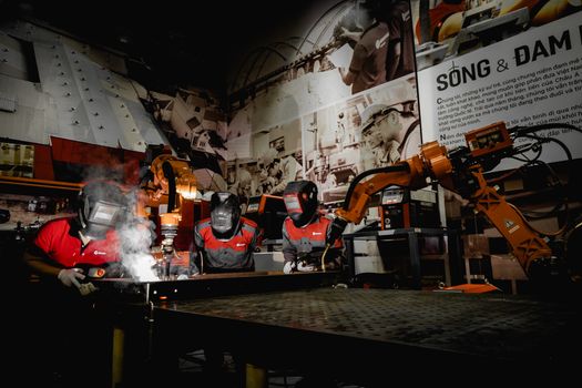 Three welders in protective gear working with robots in a high-tech industrial workshop.