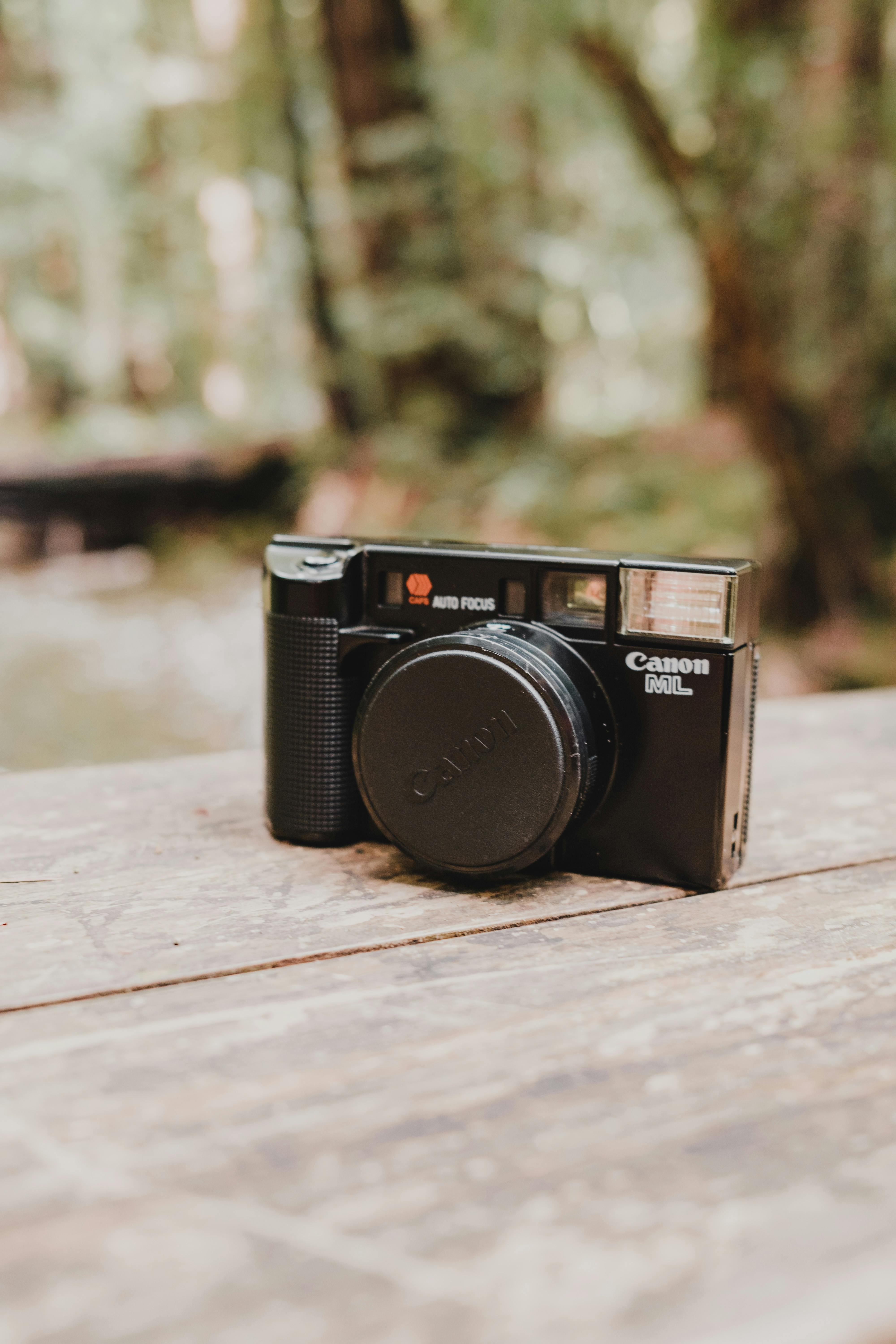 Close-up of a vintage Canon film camera on a rustic wooden table outdoors.