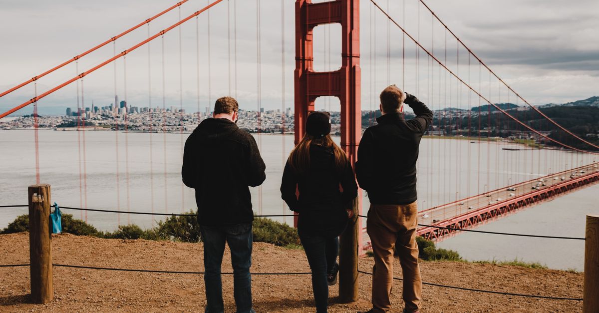 Three individuals admire the Golden Gate Bridge from a scenic viewpoint on a cloudy day.