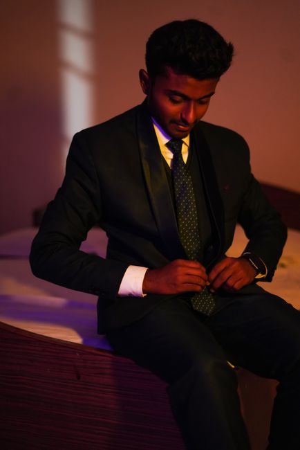 Stylish portrait of a young man in a black suit sitting indoors, exuding confidence and elegance.