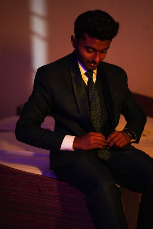 Free Stylish portrait of a young man in a black suit sitting indoors, exuding confidence and elegance. Stock Photo