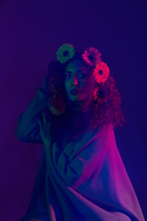 Young Woman with Flowers in Hair Posing in Studio in Purple Lighting 