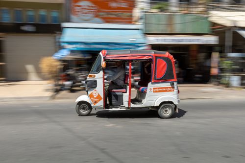 Free A fast-moving tuk-tuk drives through a bustling city street, capturing urban life in motion. Stock Photo