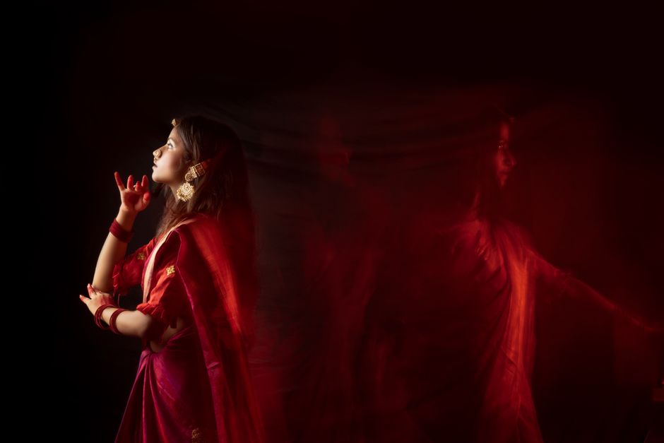 Graceful woman in traditional red saree posing artistically with dramatic lighting.