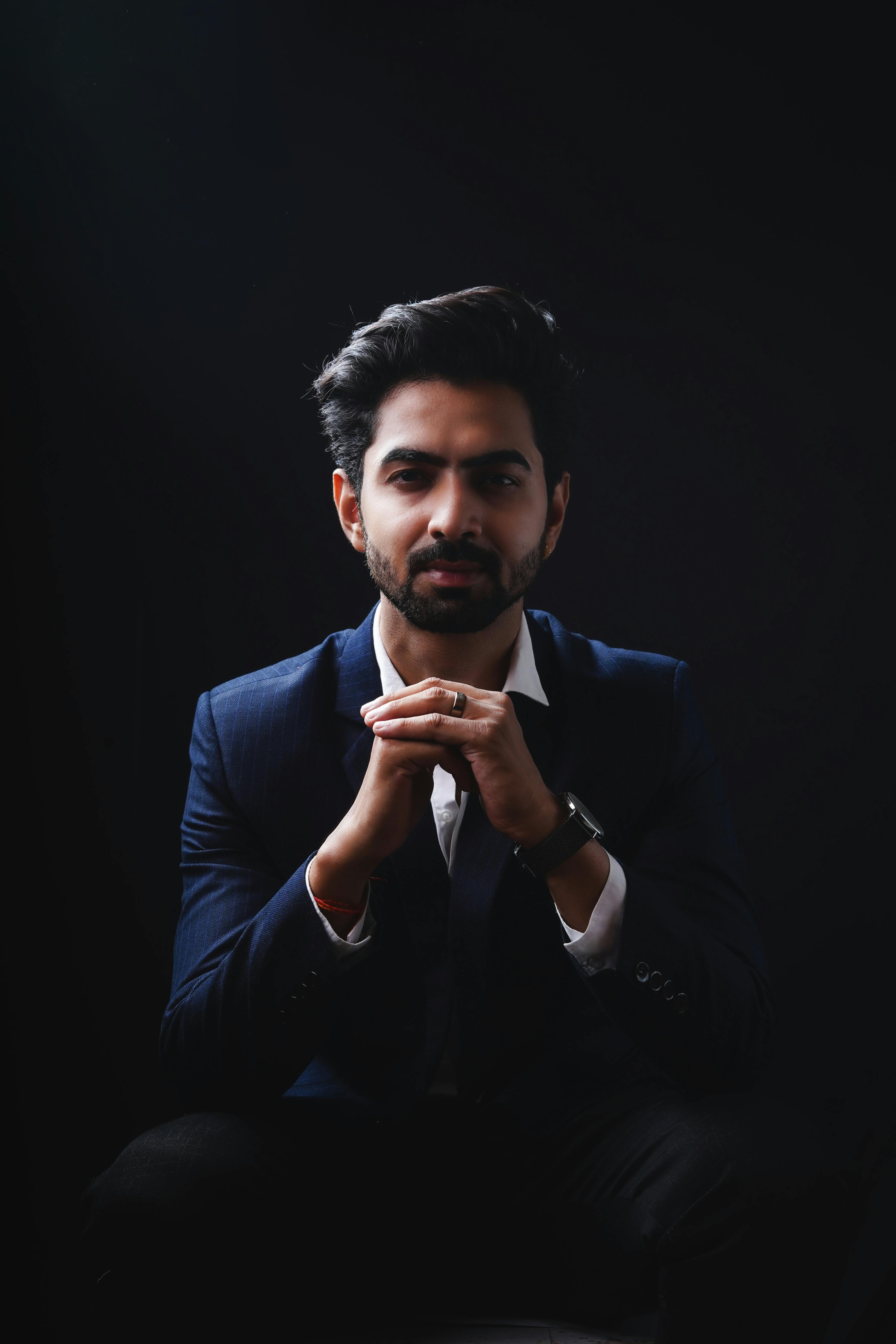 A stylish portrait of a man in a blue suit against a black background, with a contemplative pose.
