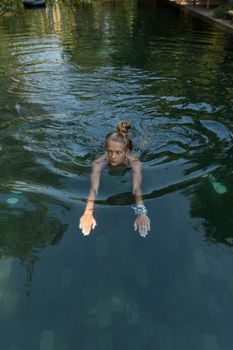 A woman swimming in a peaceful outdoor pool, surrounded by nature, exuding relaxation.