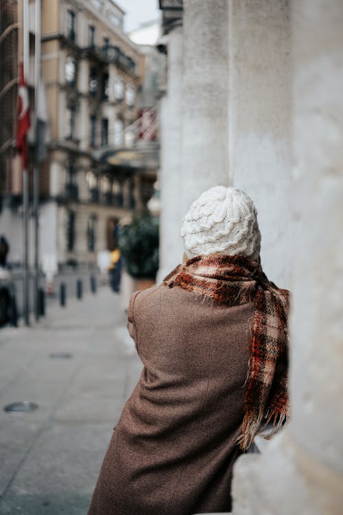 Back View of a Woman in a Coat, Scarf and Hat Walking on a Sidewalk in City 