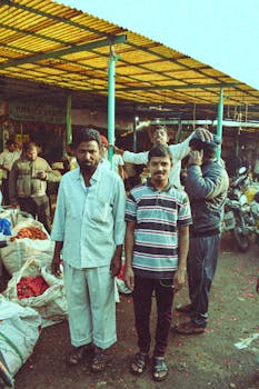 A bustling outdoor market with vendors and shoppers standing by their stalls filled with fresh produce.