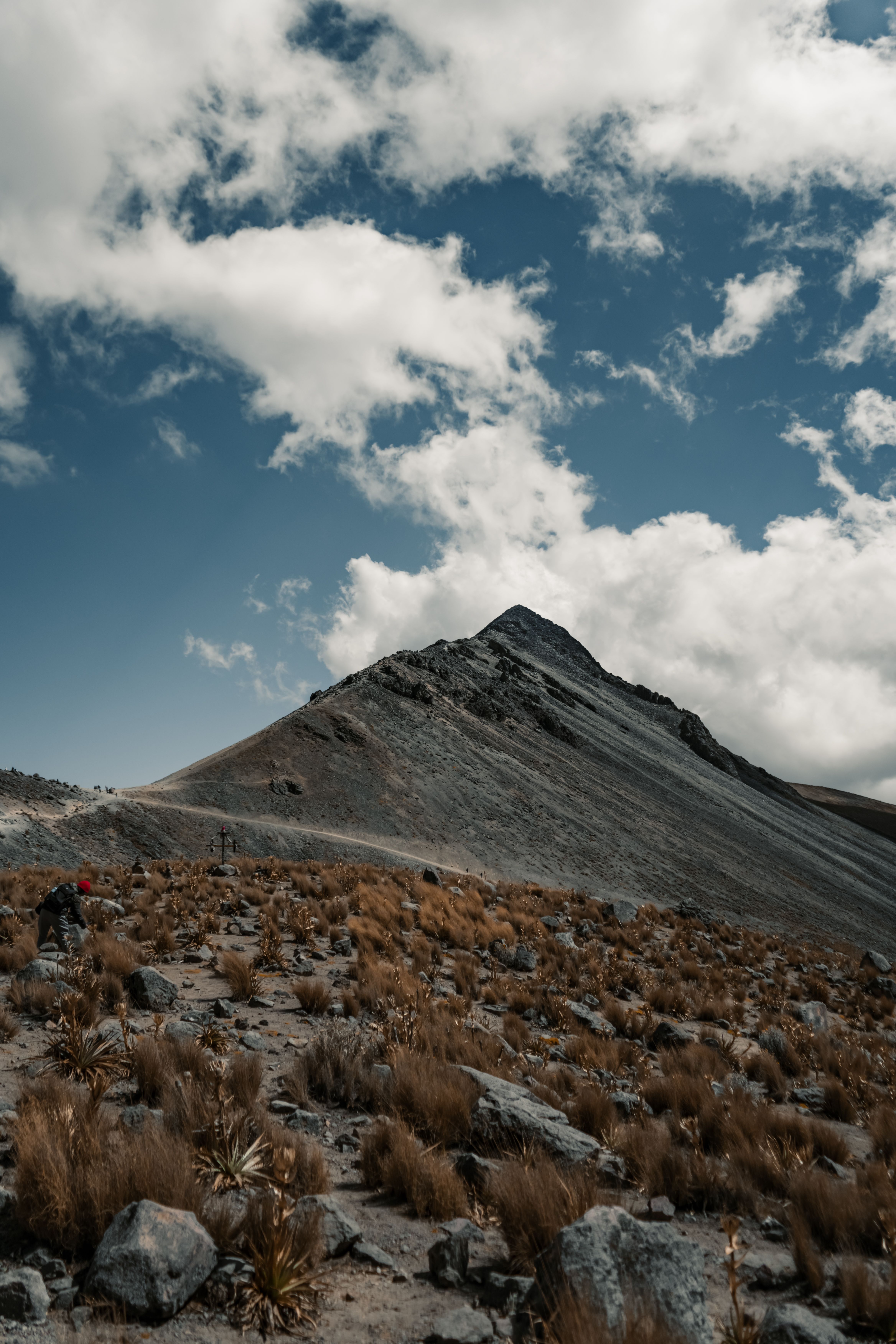 A person walking up a mountain with clouds in the sky · Free Stock Photo