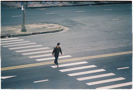 High angle view of a man walking across an empty city street at a zebra crossing.