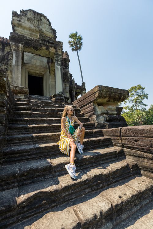 Free A young woman sits on ancient steps at Angkor Wat, enjoying a sunny day at this iconic Cambodian landmark. Stock Photo