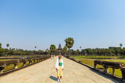 Free A lone woman stands before the majestic Angkor Wat temple under a clear blue sky, symbolizing travel and exploration. Stock Photo