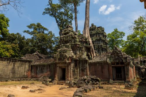 Free Explore the ancient temple ruins surrounded by lush trees under a serene blue sky, capturing nature's encroachment on history. Stock Photo