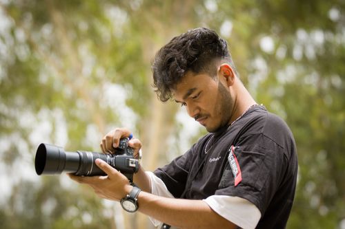 Free A young male photographer setting up his camera outdoors, focused and ready to capture the moment. Stock Photo